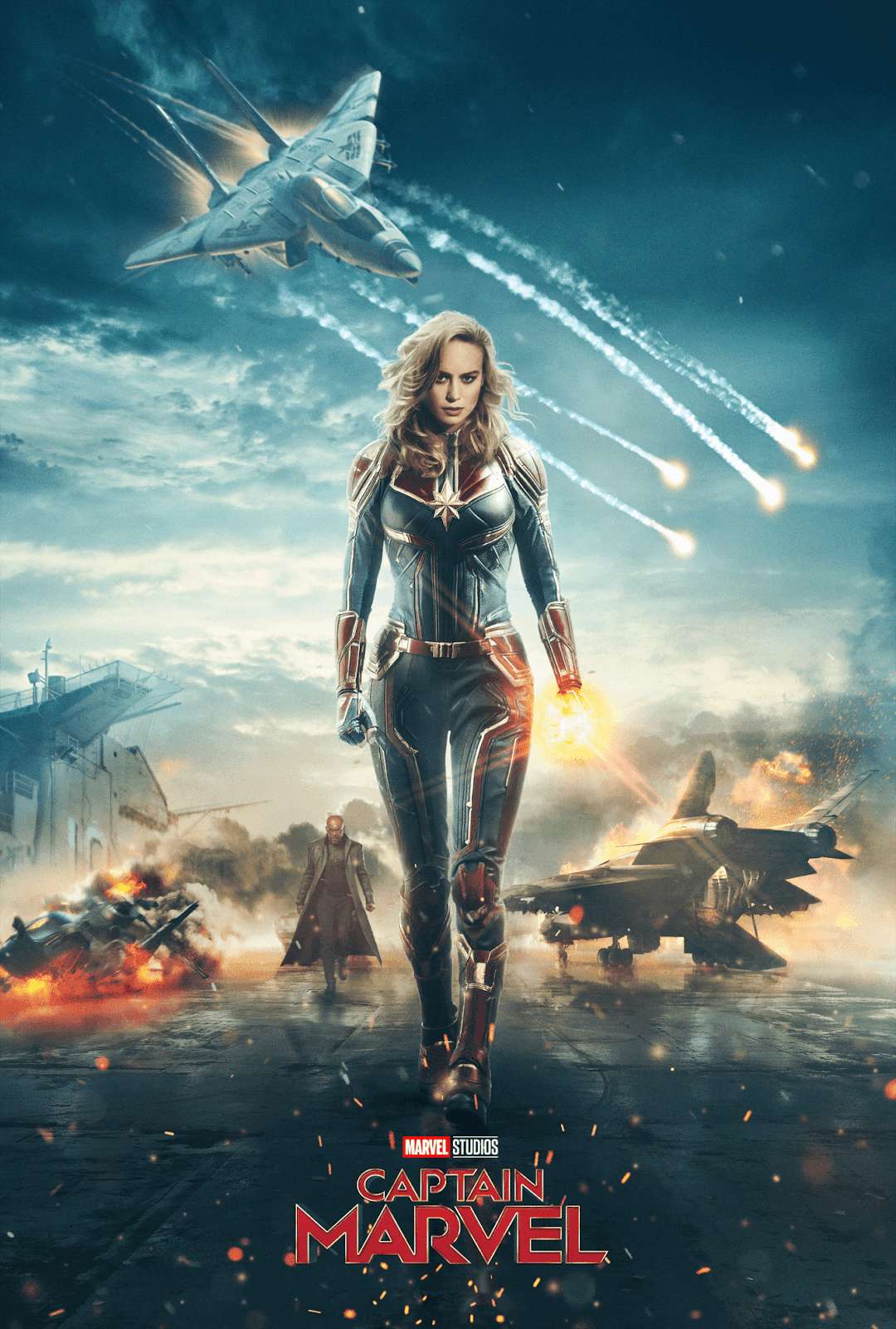Captain Marvel stands confidently in a war-torn hangar with jets flying overhead and explosions behind her. — Fighter Jets Background