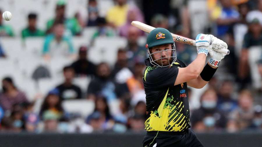 Cricket player swinging bat at ball during daytime match with crowd in background. — Finch Background
