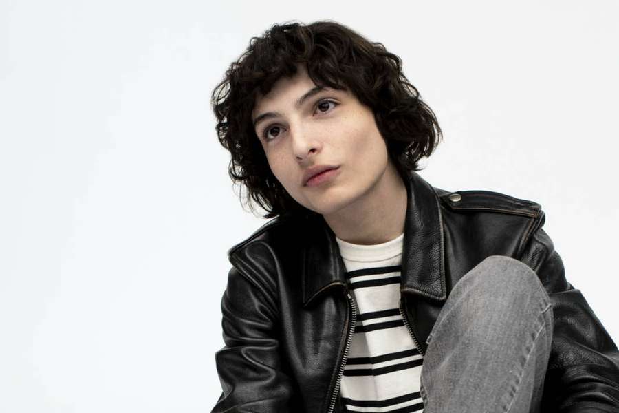 Junge Person in Lederjacke und gestreiftem Hemd, sitzend vor weißem Hintergrund — Finn wolfhard Wallpaper