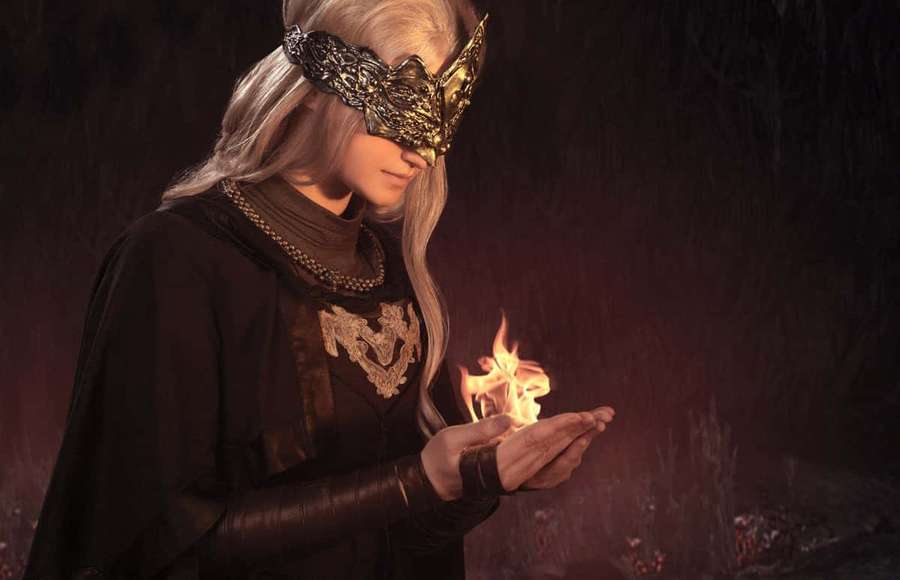 A masked elf in dark robes holds a small flame in a gloomy forest. — Fire Keeper Wallpaper
