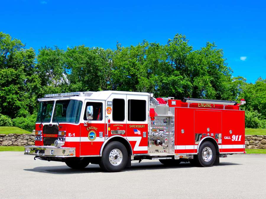 Red fire engine parked on pavement with green trees and blue sky background. — Fire Truck Wallpaper