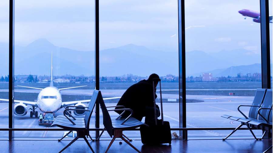 Silhouette of a traveler with suitcase watching airplane at airport window — Flight Background