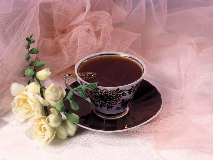 An ornate teacup with dark tea beside pale yellow roses on pink tulle. — Floral Tea Wallpaper