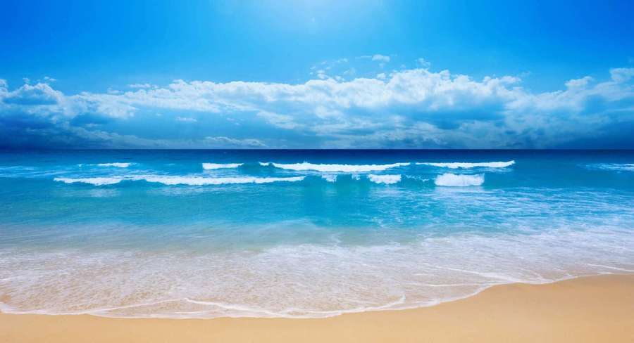 Olas turquesa del océano rompen suavemente en la arena dorada bajo un cielo azul brillante con nubes blancas. — Fondods de playa lindos Fondos de pantalla