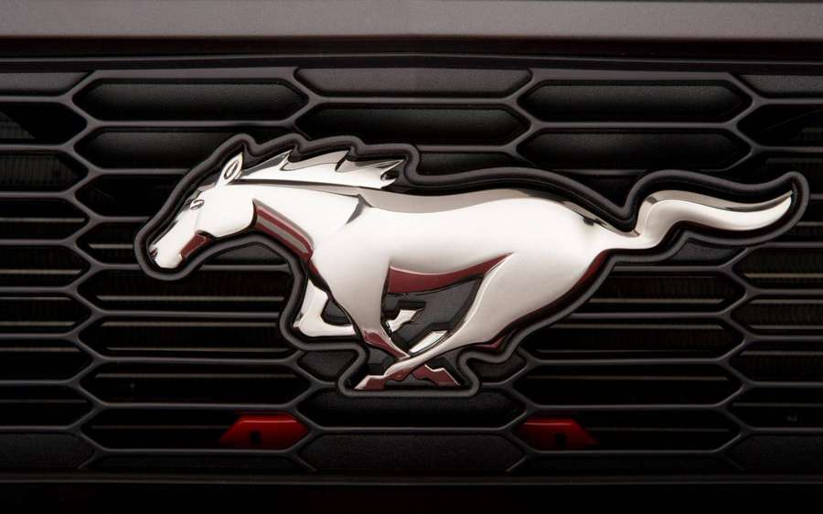 Chrome Mustang horse emblem on black car grille with red accents. — Ford Mustang HD Wallpaper