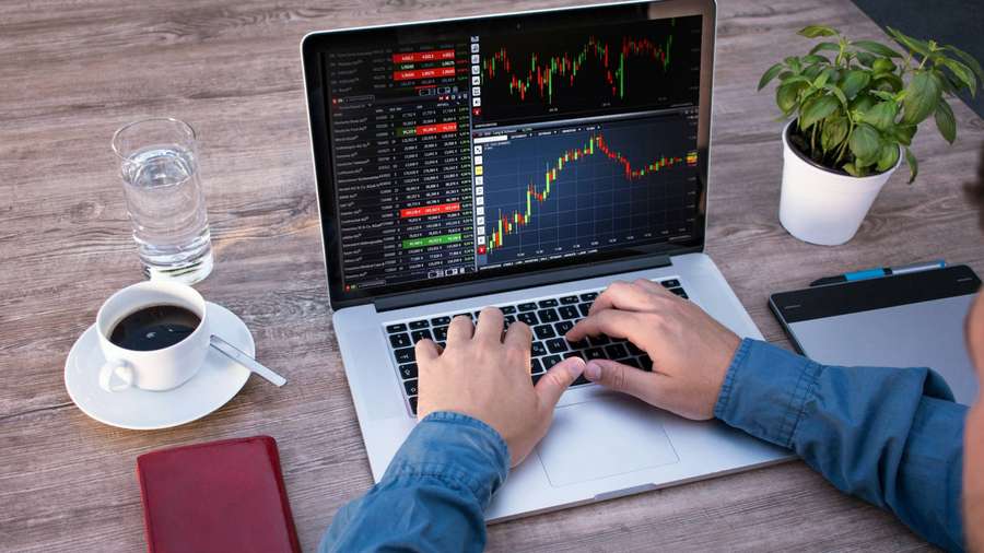 Person trading stocks on laptop with coffee and plant on wooden desk — Forex Wallpaper