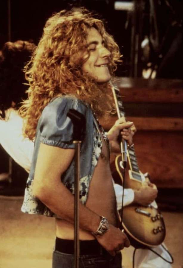 Un musicista dai capelli ricci sorride mentre suona la chitarra sul palco. — Foto di Robert Plant Immagine