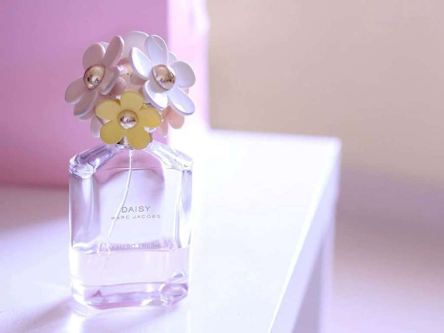 A daisy perfume bottle with pastel flowers on a white surface. — Fragrance Wallpaper
