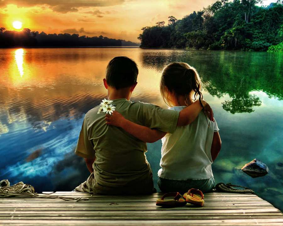 Two children sitting on a dock at sunset, arms around each other, watching the water. — Friend Picture