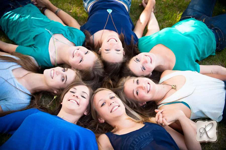 Six happy young women lying in a circle on grass smiling up at the camera. — Friends Picture