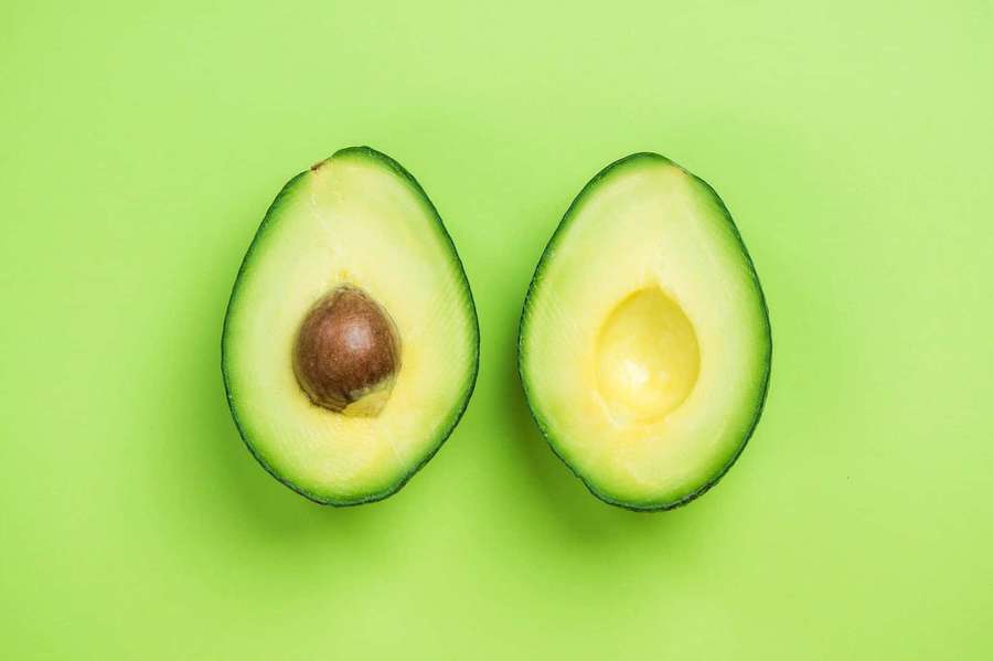 Two halves of a ripe avocado on a green background. — Fruit Picture