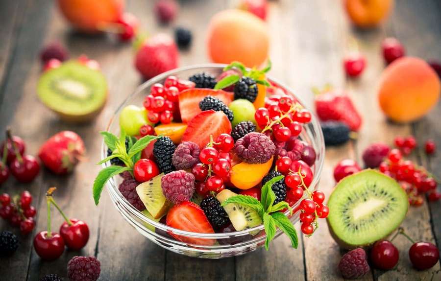 Uma tigela colorida de frutas frescas variadas sobre uma superfície de madeira. — Fundo de salada Papéis de Parede