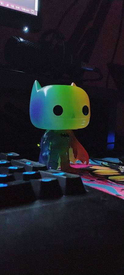 Rainbow Batman Funko Pop on a lit keyboard in a dark gaming setup. — Funko Wallpaper
