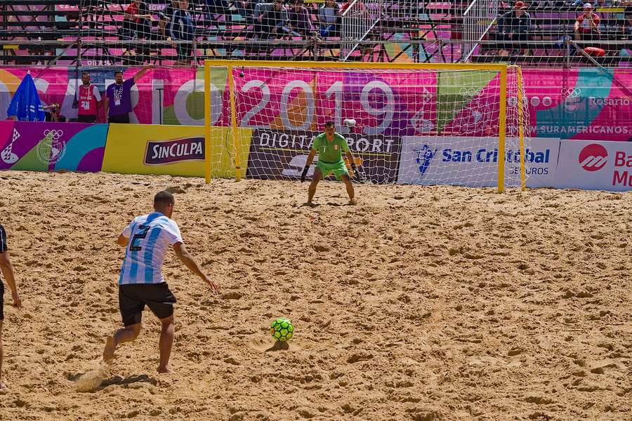 Jugador de fútbol playa patea balón hacia portero durante partido diurno. — Fútbol Playa Fondos de pantalla