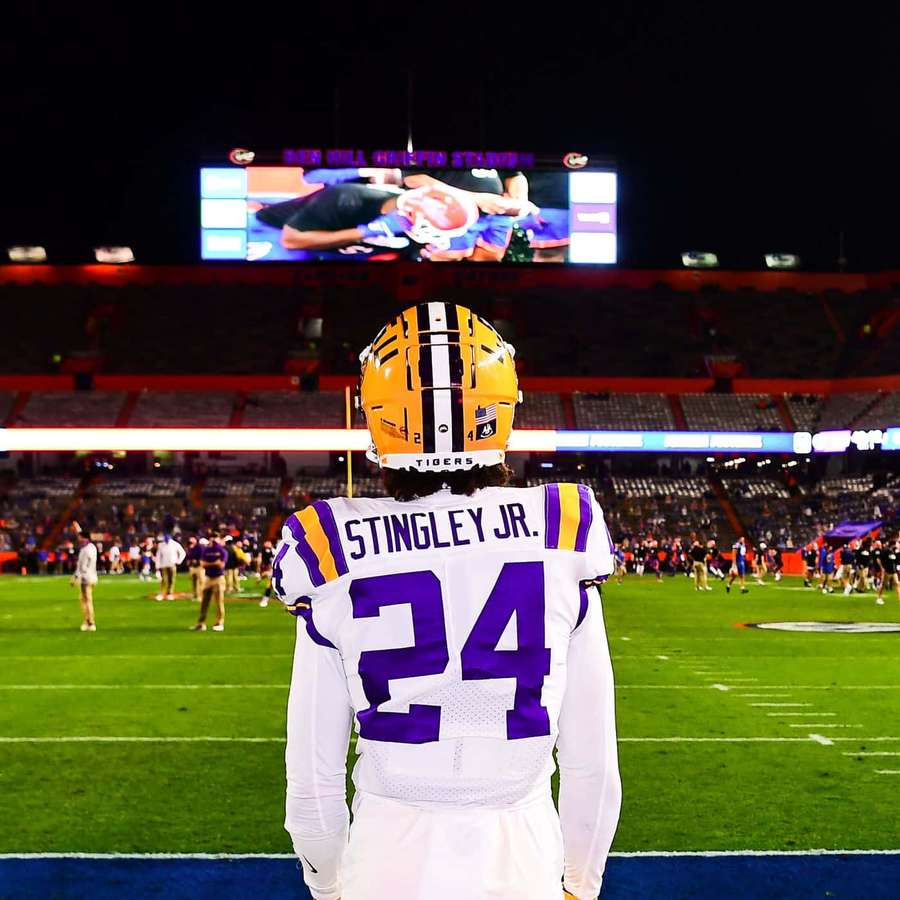 Jogador de futebol americano número 24 com uniforme branco e roxo em campo à noite de frente para o placar. — Futebol da Lsu Papéis de Parede