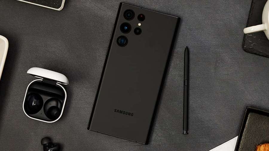 Black Samsung phone with S Pen and earbuds on a dark gray desk surface. — Galaxy S25 Wallpaper