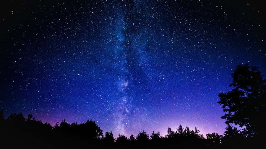Milky Way galaxy above forest at night with vibrant blue and purple hues. — Galaxy Sky Background