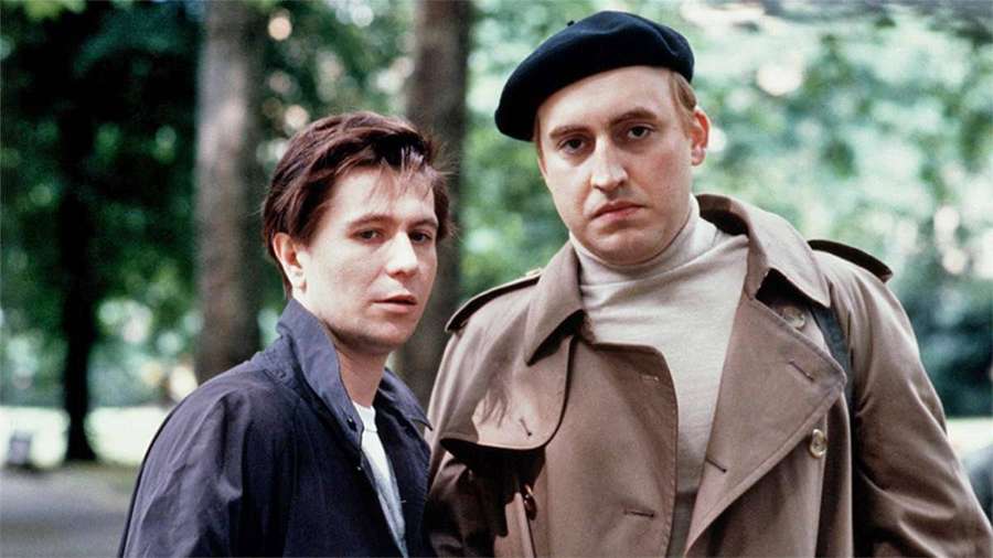 Two men in a park one wearing a beret and trench coat — Gary Oldman Background