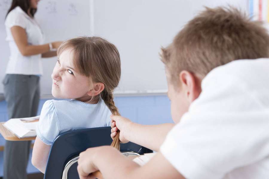 Mädchen starrt Jungen an, der an ihren Haaren im Klassenzimmer zieht. — Gemein Wallpaper