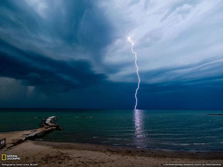 Lightning strikes the ocean during a stormy night over a beach. — Geographic Background