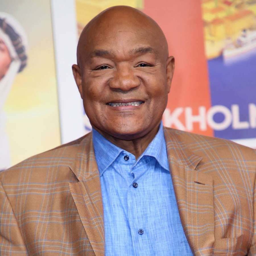 Kahlköpfiger Mann in kariertem Blazer und blauem Hemd lächelt bei einem Event. — George Foreman Bilder
