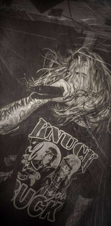 A tattooed rock musician screams into a mic on stage in black and white. — Ghostemane Background