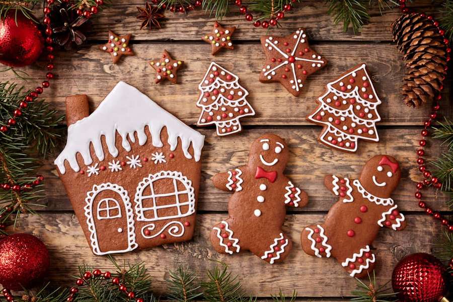 Gingerbread cookies shaped like a house trees and people on a wooden table with pinecones and red ornaments. — Gingerbread Background