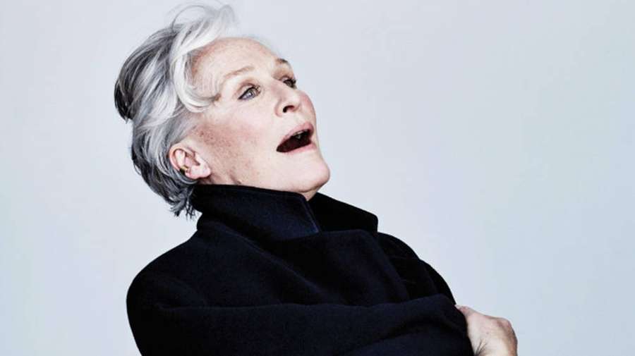 A woman with silver hair and black coat looking upward with expressive face. — Glenn close Wallpaper