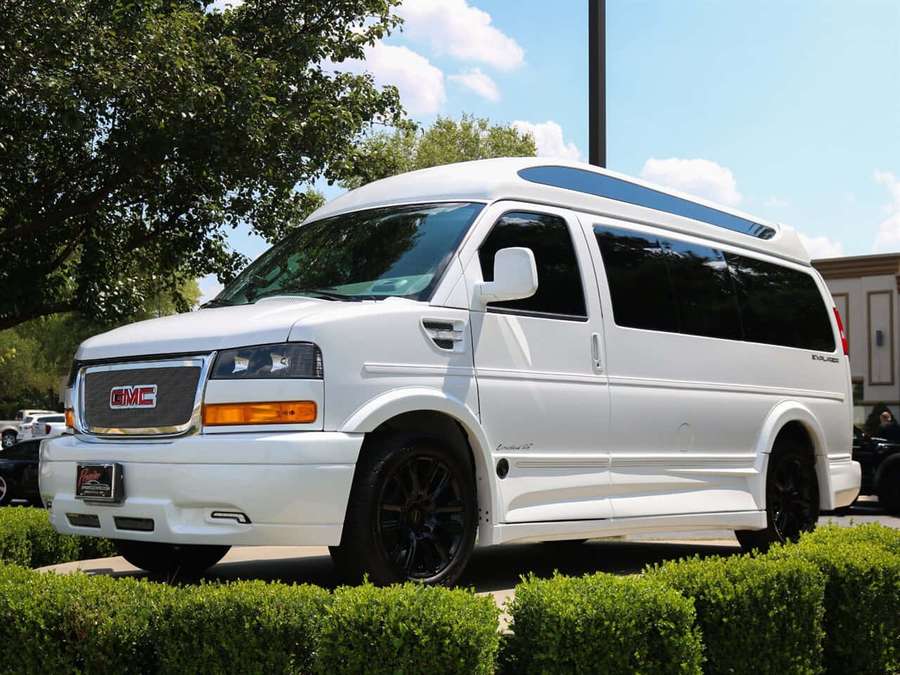 White GMC van with black rims parked outdoors near green hedges on a sunny day. — Gmc Savana Wallpaper