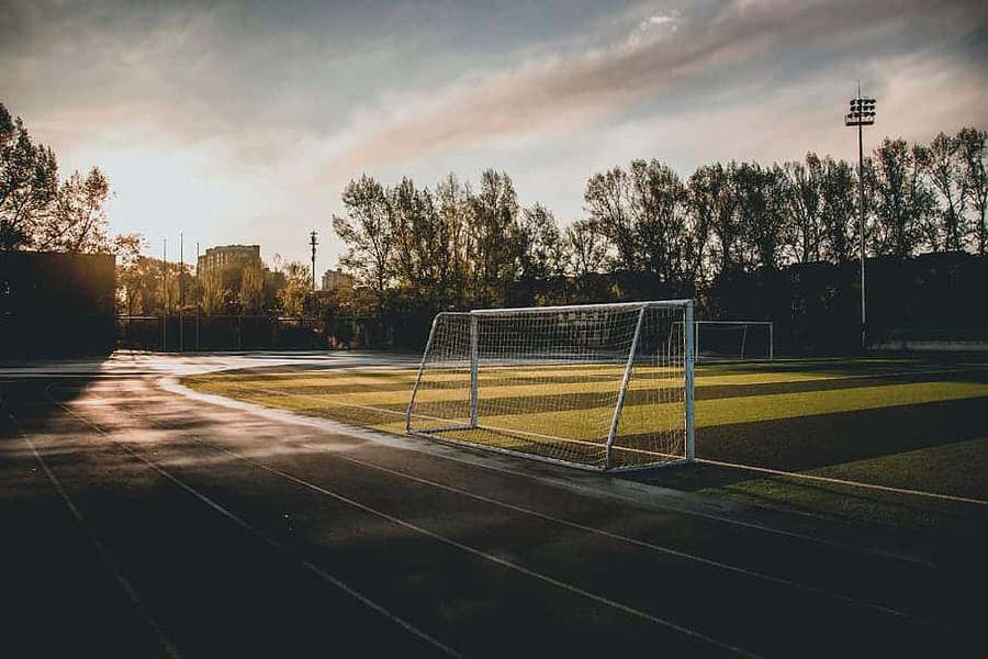An empty soccer field at sunset with a goal net and track in shadow. — Goal Post Wallpaper