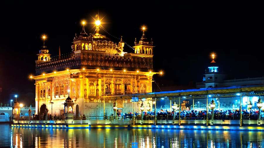 Goldener Tempel, der nachts leuchtet, mit Spiegelungen im Wasser und Menschen in der Nähe. — Goldener Tempel Bilder Wallpaper