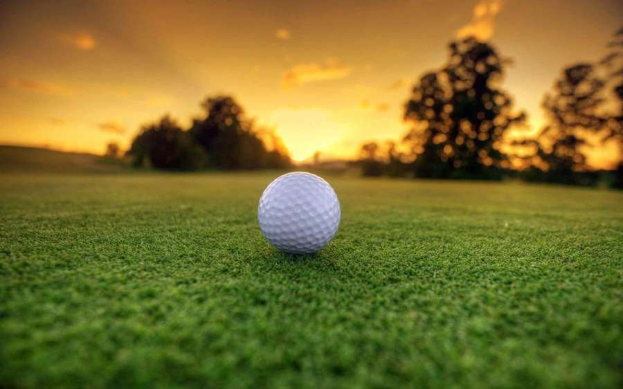 Golf ball on green grass at golden sunset — Golf Background
