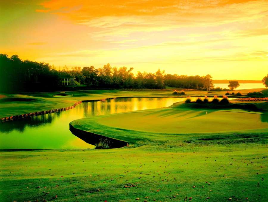 Golf course at sunset with green fairways and water hazard reflecting golden sky. — Golf Course Background