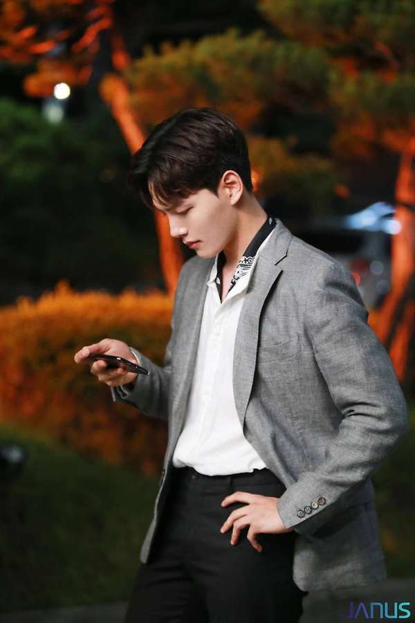 Young man in gray blazer looking at phone under warm night lights. — Goo Wallpaper