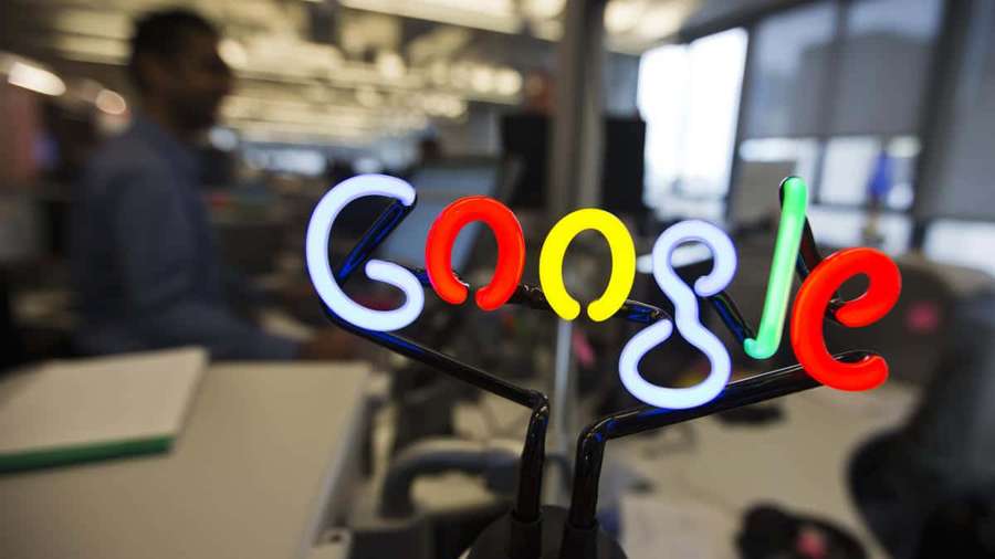Neon Google logo on desk in modern office with blurred worker behind. — Google Picture