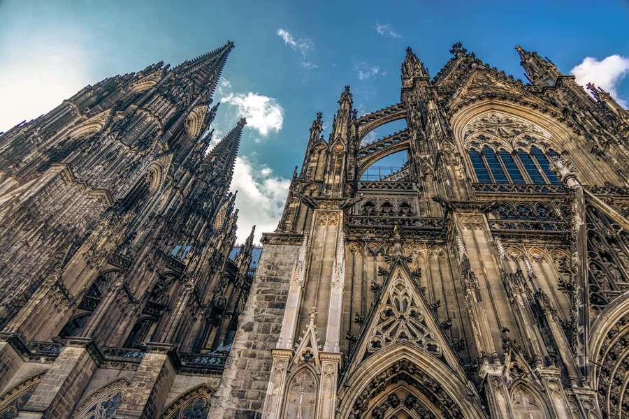 Cologne Cathedral's Gothic spires and detailed facade under a blue sky with clouds. — Gothic Architecture Wallpaper