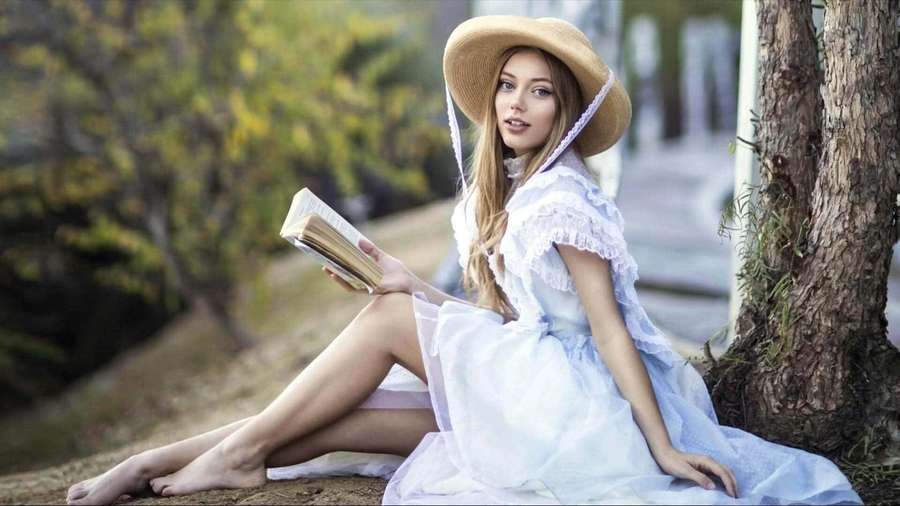 Young woman in blue dress and straw hat reading book under tree in forest. — Grace Van Dien Wallpaper