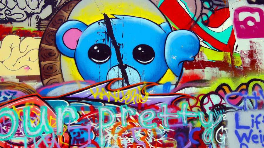 Blue cartoon bear graffiti mural with colorful tags on a city wall. — Graffiti Wall Background