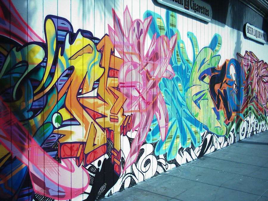 Bunte Graffiti-Kunst an einer Stadtmauer mit Gehweg im Vordergrund. — Graffiti wand Wallpaper