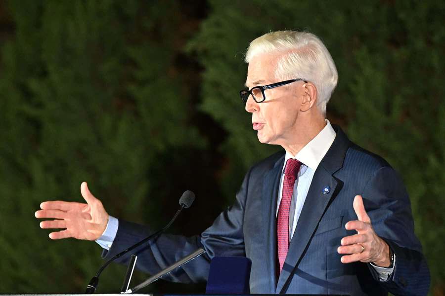 Man in suit giving speech at outdoor podium with greenery behind him. — Gray Davis Wallpaper
