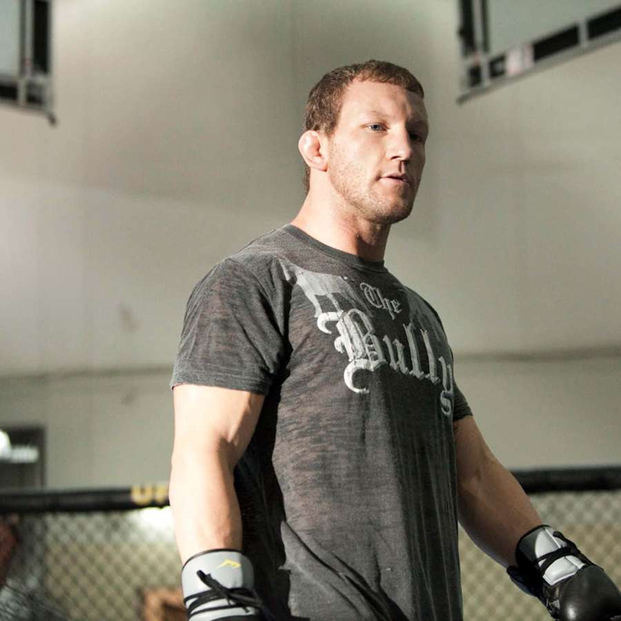 A focused MMA fighter in a grey t-shirt and gloves inside a cage. — Gray Maynard Wallpaper