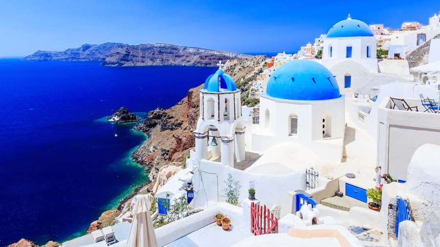 Santorini's blue-domed churches and white buildings on a cliffside overlooking the sea. — Greece Background