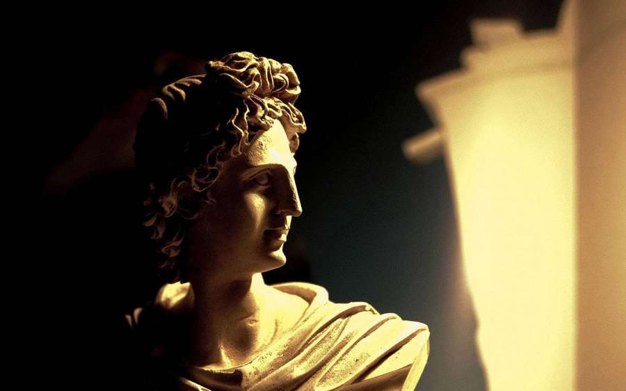 Classical marble bust illuminated by warm light in a dark museum setting. — Greek Statue Background