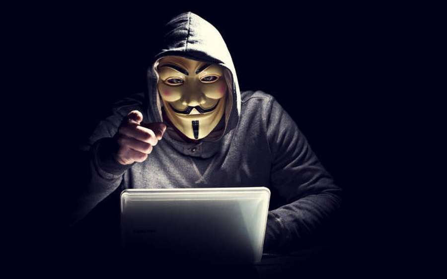 Person mit Guy-Fawkes-Maske zeigt auf Laptop in dunklem Raum. — Hacker 3d Wallpaper