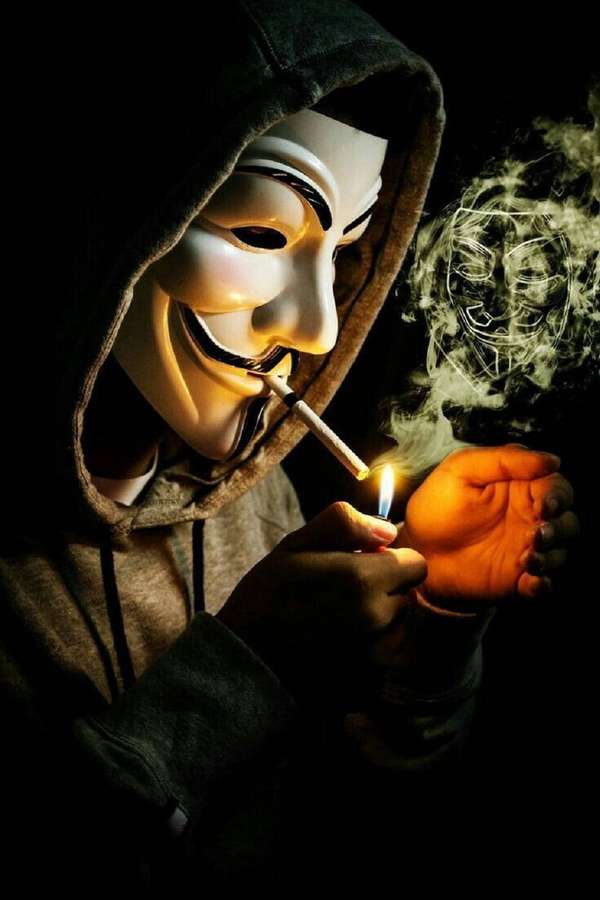 Person in Guy-Fawkes-Maske zündet Zigarette mit Feuerzeug an, Rauch bildet Maske. — Hacker Mask Bilder