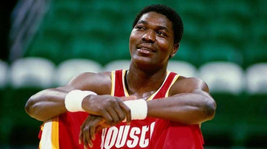 Houston Rockets basketball player smiling with arms crossed in arena. — Hakeem Olajuwon Background