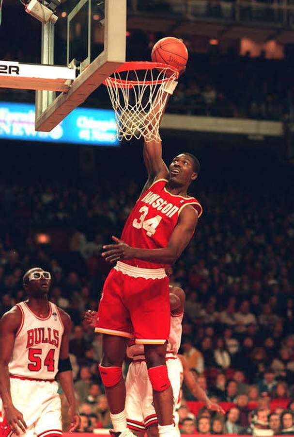 Basketball player in red uniform dunks ball during game with crowd in background. — Hakeem Olajuwon Wallpaper