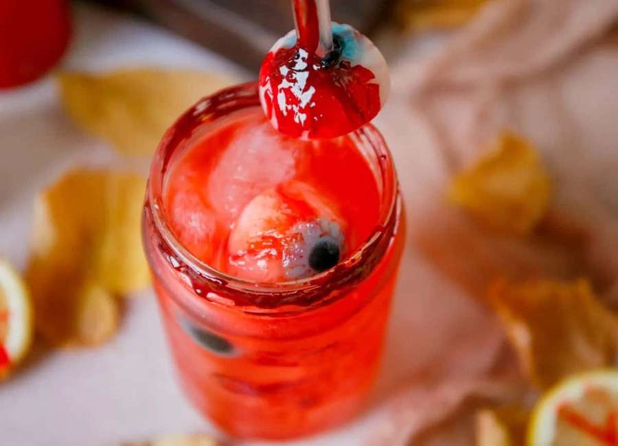 A red cocktail with a gummy eyeball garnish and lemon wedges. — Halloween Drinks Wallpaper