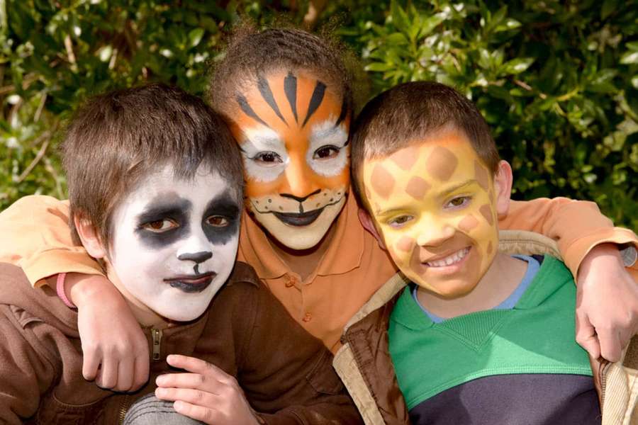 Three kids with animal face paint hugging in a garden. — Halloween Face Paint Wallpaper