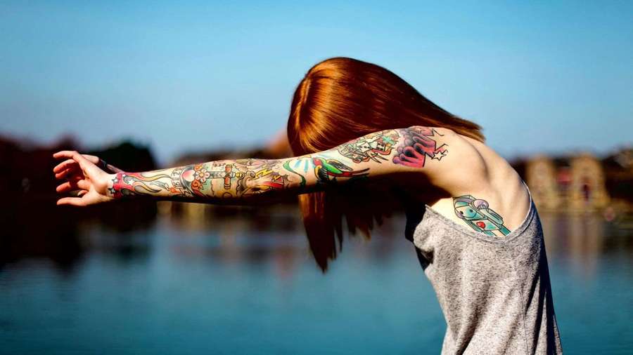 Person with colorful tattoos stretching by a lake at sunset. — Halloween Tattoos Wallpaper